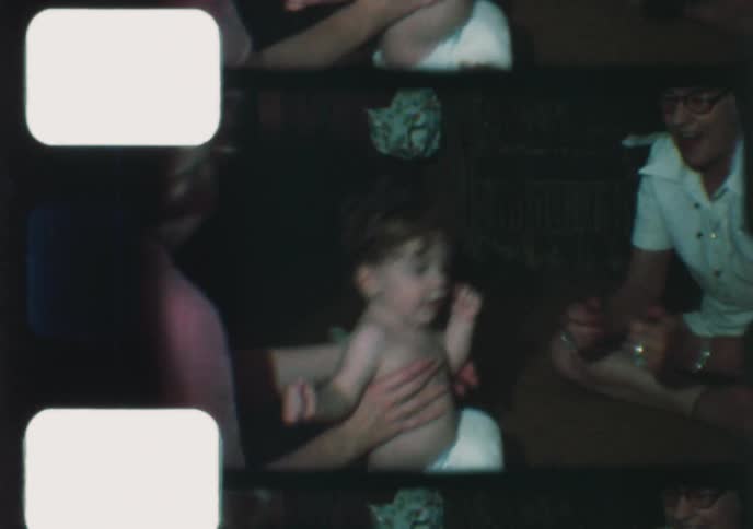 Nostalgic 1970s home movie footage shows a cute toddler with curly hair taking their first wobbly steps between their mother and grandmother
