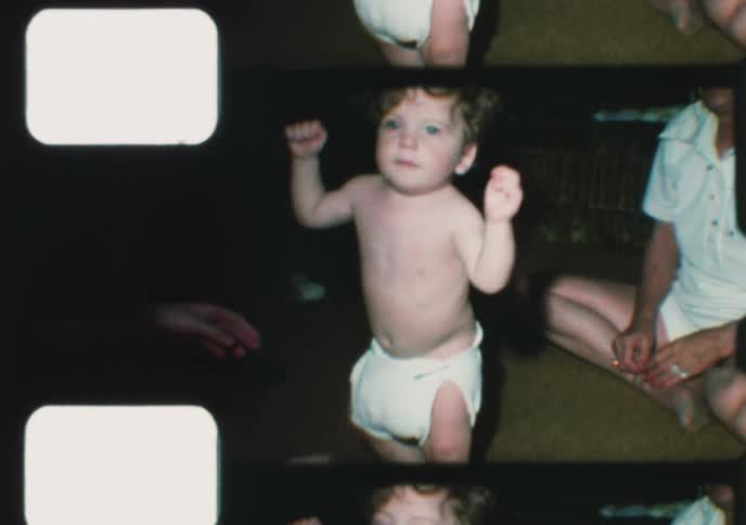 Vintage home movie captures an adorable baby with curly hair learning to stand with help from its mother and grandmother