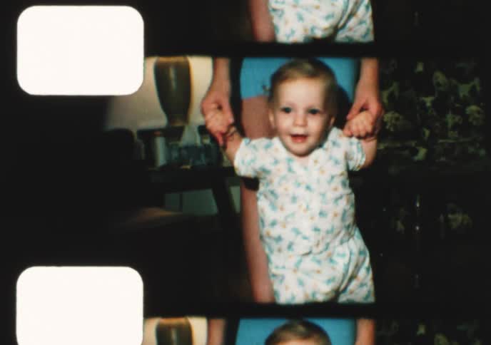 A proud mother helps her smiling baby boy take his first steps and crawl across the floor in a vintage home movie from the 1970s