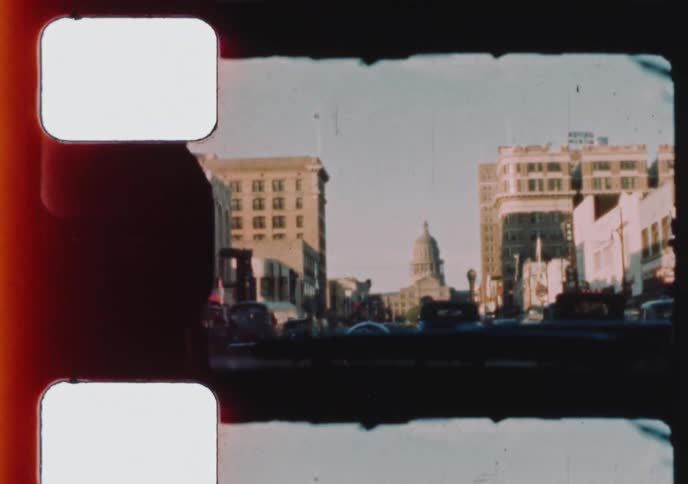 Archival 8mm film shows a view from a car driving down a city street with the State Capitol building in the distance