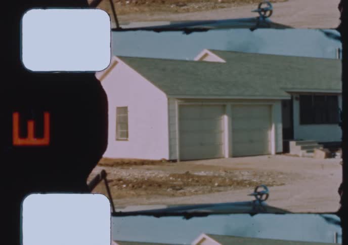 Archival 8mm film pans across a modest suburban home with a two-car garage and a dirt yard in the 1950s