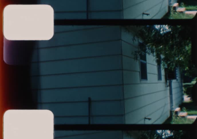 Vintage home movie footage captures a quiet suburban house with a classic car parked in the driveway on a sunny day