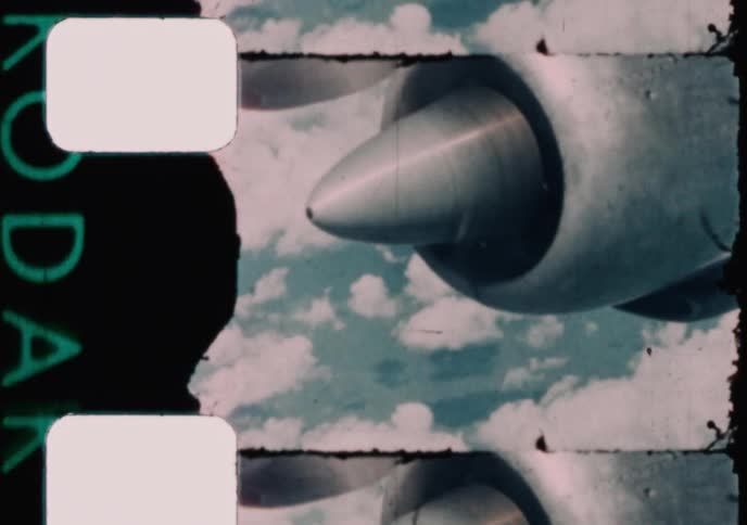 Vintage 16mm film footage shows the engine and spinning propeller of an airplane flying high above the clouds