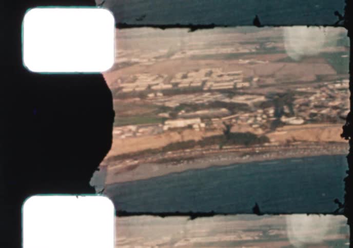 An aerial flyover of a bustling coastal city and its arid landscape, captured on grainy vintage film