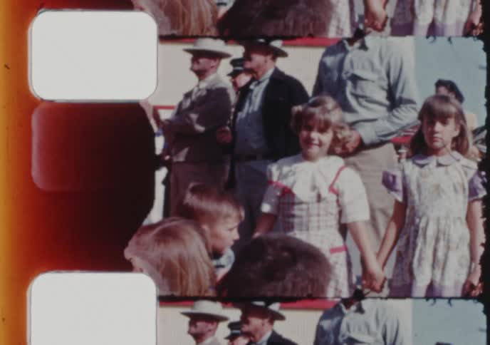 Vintage film strip footage shows two young sisters holding hands while watching a parade with their family
