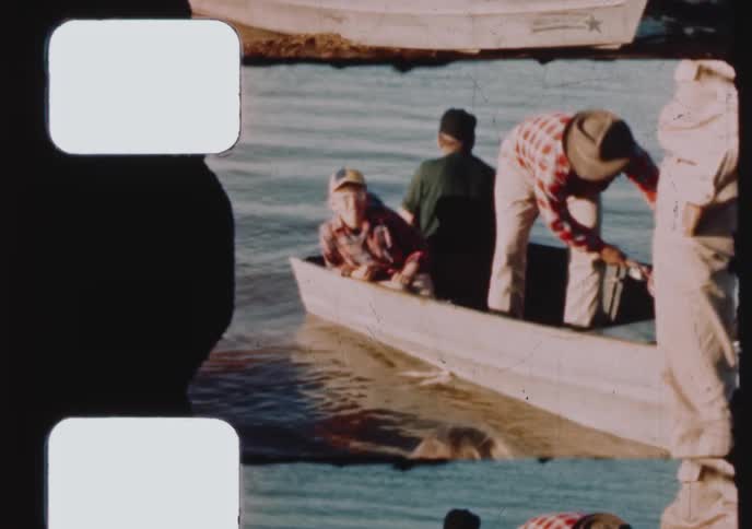A father and his two sons enjoy a fishing trip on a lake, pulling their boat ashore and showing off their catch in this vintage home movie