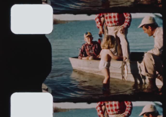 Archival footage captures a curious toddler holding a freshly caught fish while standing in a lake next to their family's boat