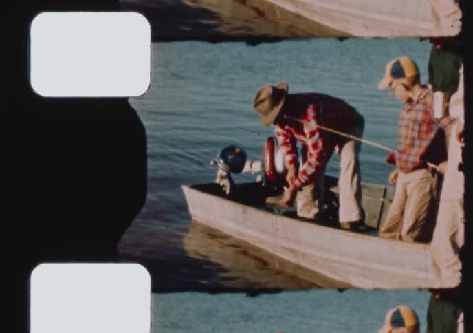 Vintage footage shows a group of men and a boy preparing a small motorboat for a fishing trip on a sunny day by the lake