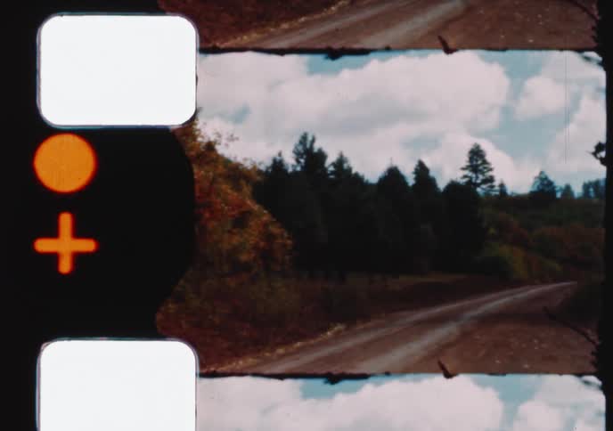 A split-screen view from vintage 8mm film pans across a winding country road through a forest with autumn foliage