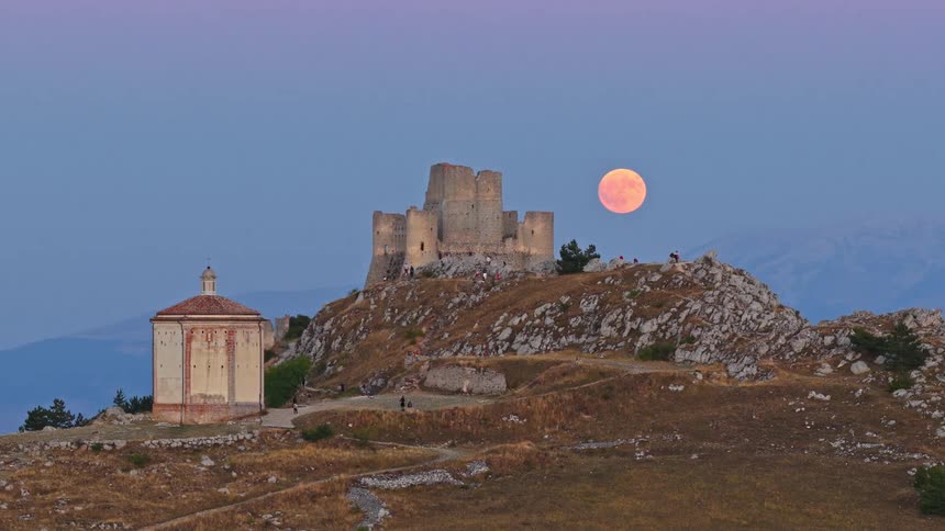 A dramatic time-lapse of a giant full moon rising over the ancient Rocca Calascio castle in the Italian mountains at dusk