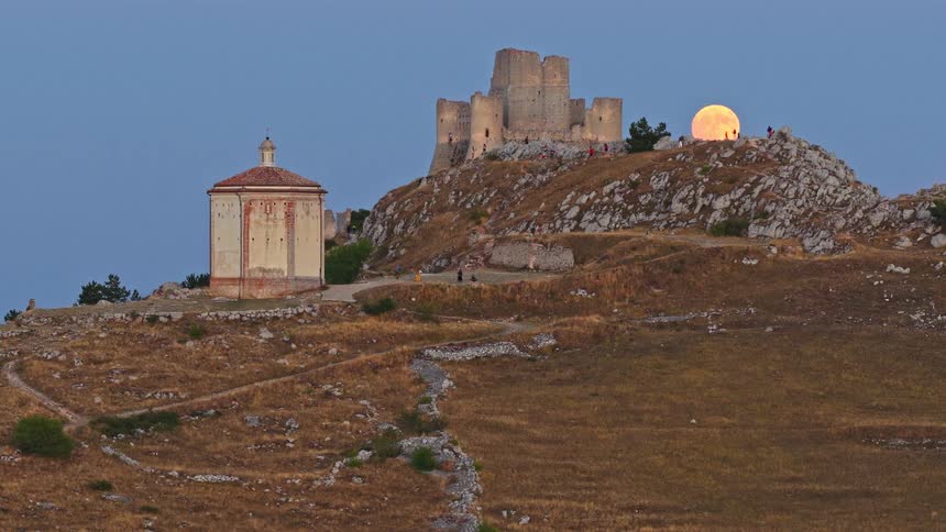 A stunning view of the full moon rising behind the medieval Rocca Calascio castle on a hilltop in Abruzzo, Italy