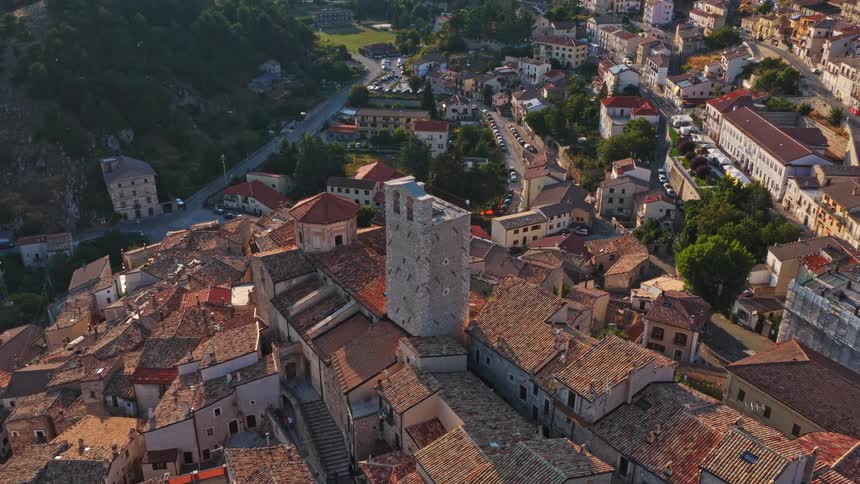 A majestic aerial view pulls back from a historic stone bell tower revealing a picturesque Italian village nestled in a valley at golden hour