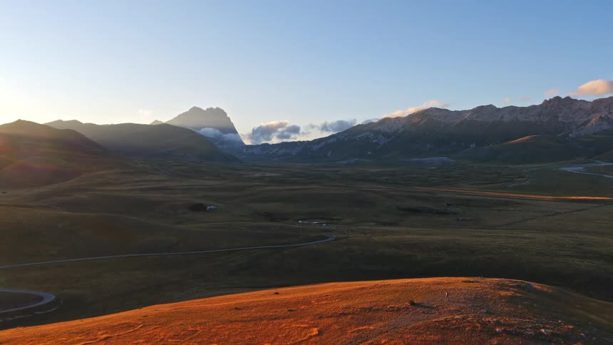 A stunning aerial view captures the golden sunrise over a vast mountain valley, revealing a winding road through the majestic landscape
