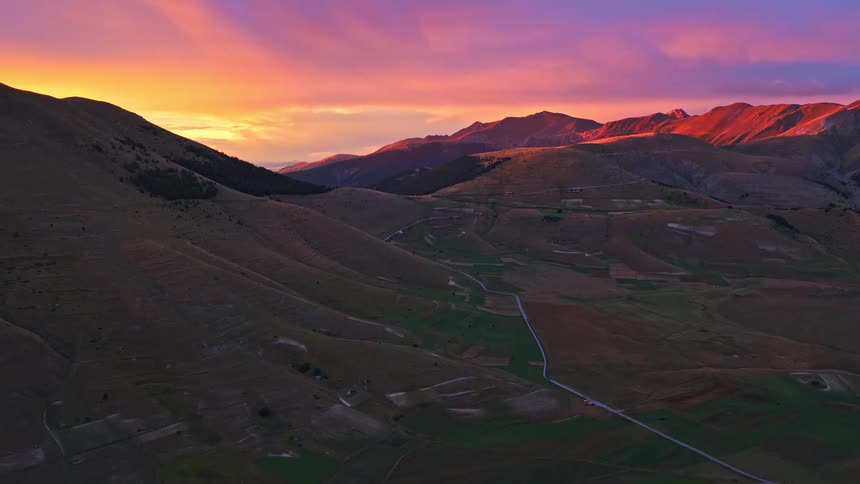 A spectacular aerial view reveals a vibrant and colorful sunset over the rolling hills and mountains of a vast valley