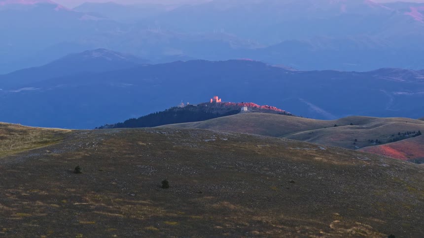 A stunning sunrise illuminates the ancient Rocca Calascio castle, gradually appearing behind rolling hills in the vast Abruzzo mountain range
