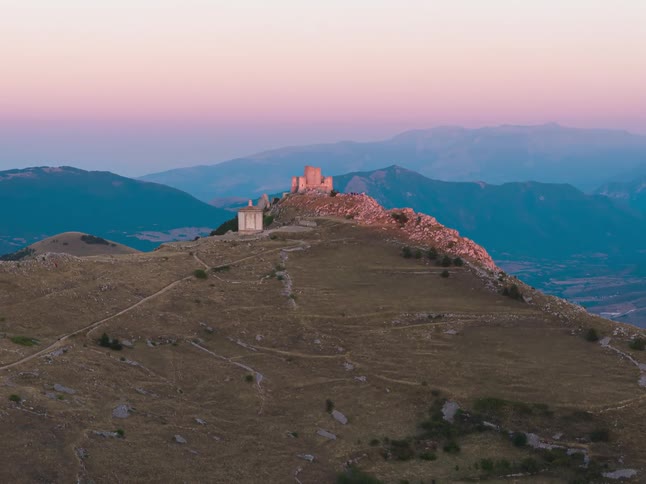 A stunning timelapse captures the transition from a golden sunset to twilight as the full moon rises over the ancient Rocca Calascio castle in the Apennine mountains of Italy
