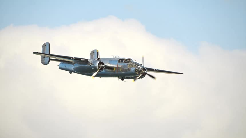Dramatic slow motion shot of a polished WWII-era B-25 Mitchell bomber flying through a cloudy sky