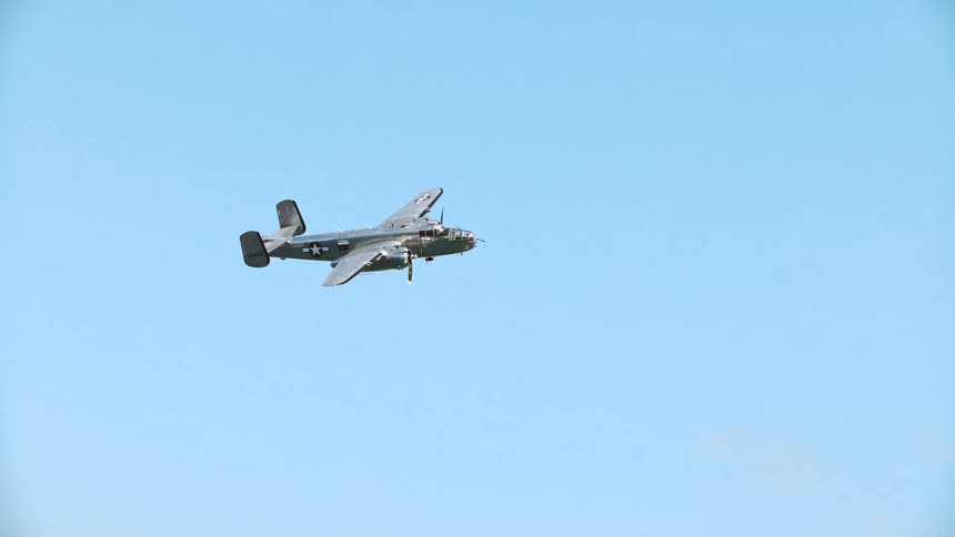 A historic World War II B-25 Mitchell bomber flies steadily across a clear blue sky
