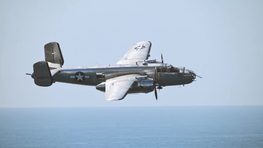 A classic World War II B-25 Mitchell bomber flies in slow motion over the open ocean