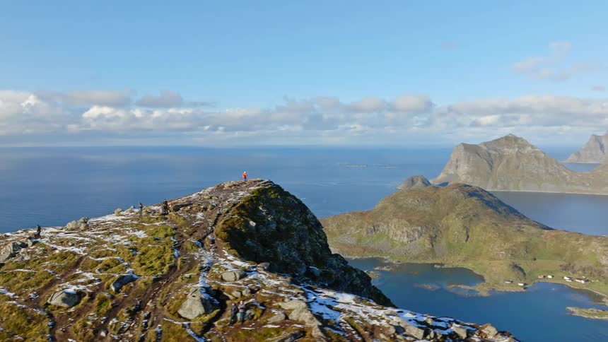 Sweeping aerial footage captures hikers admiring the majestic coastal view from a snow-dusted mountain peak in Norway