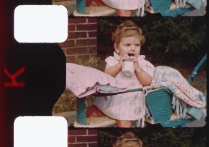 A scan of a vintage film roll captures a sweet baby girl drinking milk from a bottle in her stroller