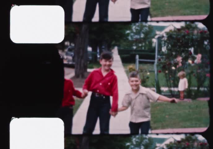 Three happy young boys hold hands and roller skate down a suburban sidewalk in a nostalgic vintage home movie