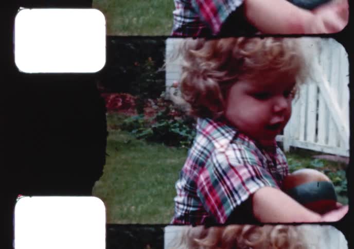 Vintage 8mm home movie of a cute toddler with curly blonde hair holding two small balls in a backyard