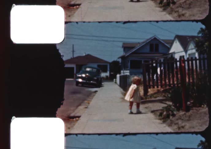 A little girl walks on a suburban sidewalk as her older brother rides past on his tricycle in this authentic vintage home movie