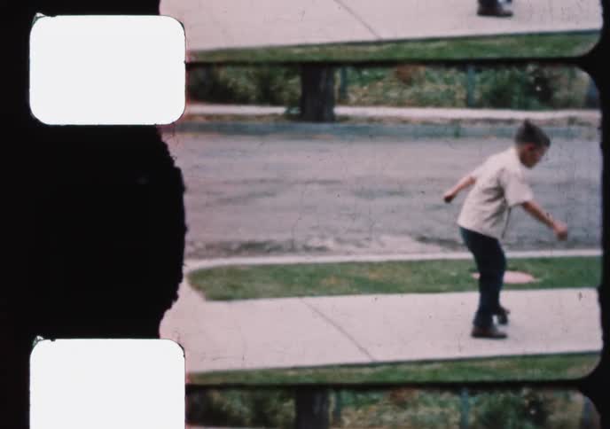 A young boy learns how to roller skate on the sidewalk in a quiet suburban neighborhood in this charming vintage home movie