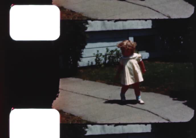 Vintage 1960s footage of a cute toddler walking on a sidewalk before falling down when a boy on a bike rides by