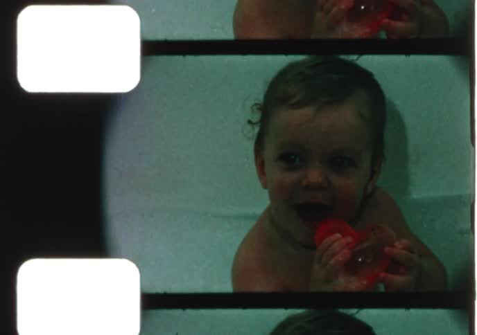 A cute baby laughs and plays with a red toy while taking a bath in this authentic vintage home movie footage
