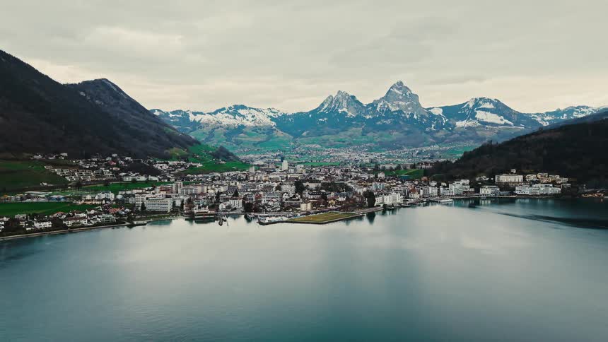 A picturesque European town sits on the shores of a tranquil lake at the foot of the snow-capped Swiss Alps