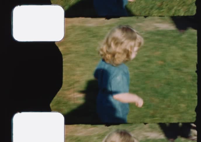 Vintage footage shows a cute toddler in a blue jumpsuit playing with a reel mower and running in a sunny backyard