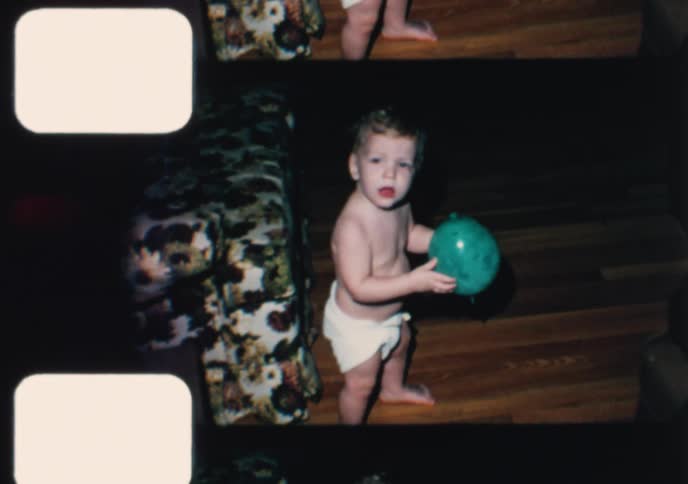 Vintage 8mm home movie footage shows a cute toddler in a diaper smiling and playing with a balloon at home
