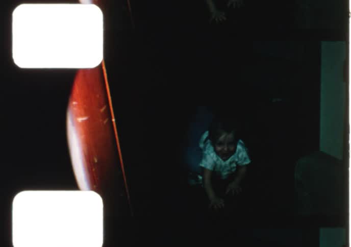 Two babies crawl and play in a dark room in this home movie from 1979