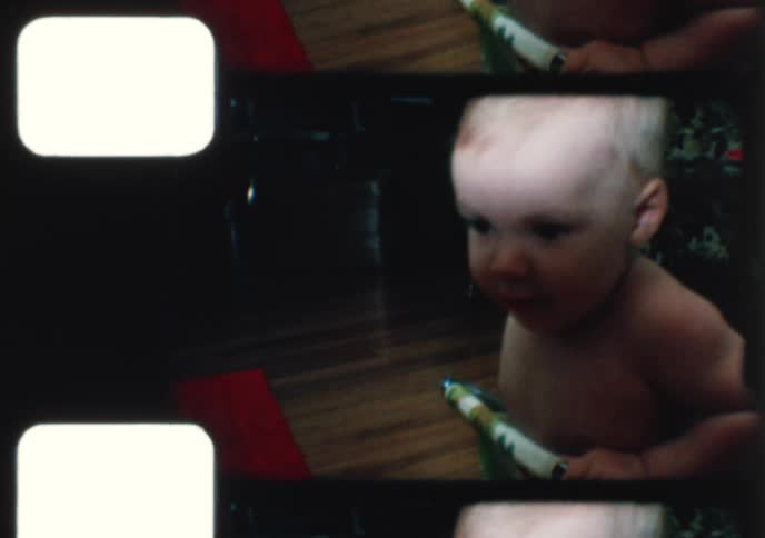 Vintage 8mm footage captures a happy baby bouncing and smiling in a retro walker inside a home