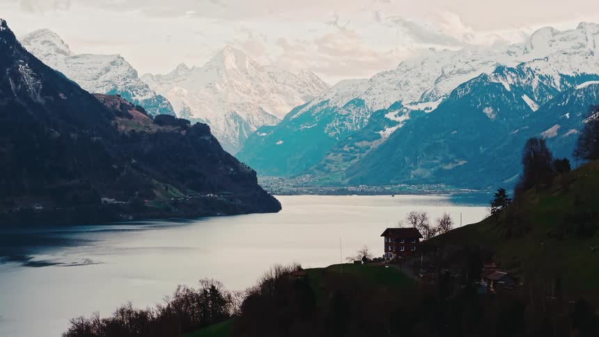 A stunning wide shot of a serene lake in the Swiss Alps, surrounded by towering snow-capped mountains and a picturesque chalet on the hillside