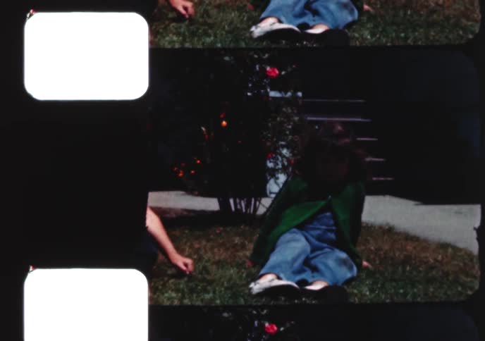 Three young siblings are captured on 8mm film sitting and standing in their suburban front yard