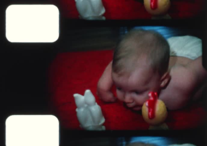 Vintage 8mm home movie footage shows a cute baby boy with blond hair enjoying tummy time on a red mat in 1968