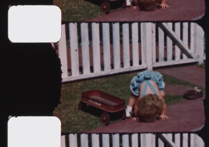 Vintage 8mm home movie captures a cute toddler in a blue bonnet and overalls playing with her red wagon and falling down in the backyard