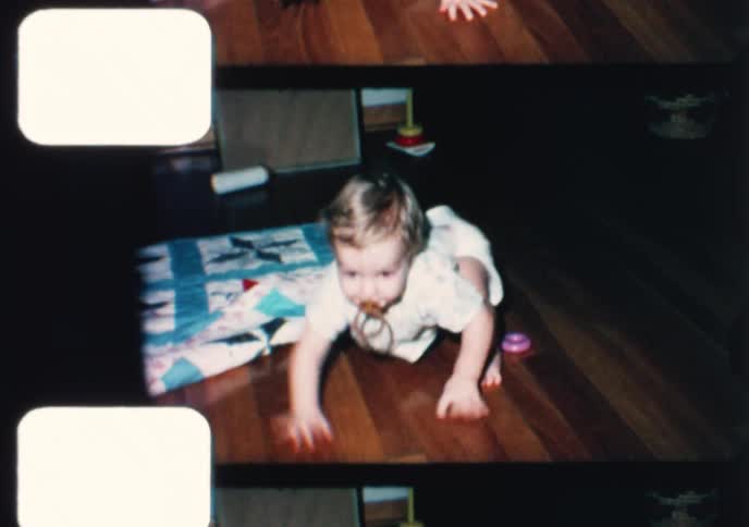 Vintage 8mm film strip captures a cute toddler with a messy face and pacifier learning to walk in a 1960s living room