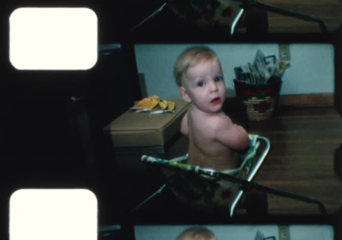 An adorable baby boy with blue eyes happily bounces and scoots around in his vintage walker in this charming home movie