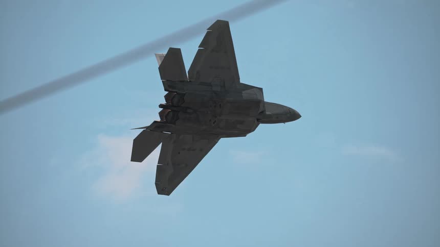 A sleek F-22 Raptor fighter jet performs a powerful vertical climb in stunning slow motion, its afterburners blazing against the blue sky