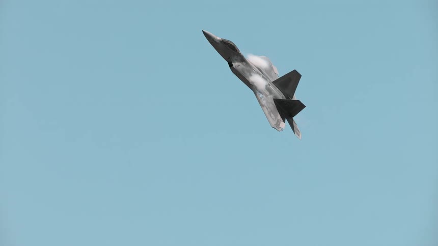 A powerful F-22 Raptor fighter jet flies in super slow motion against a clear blue sky
