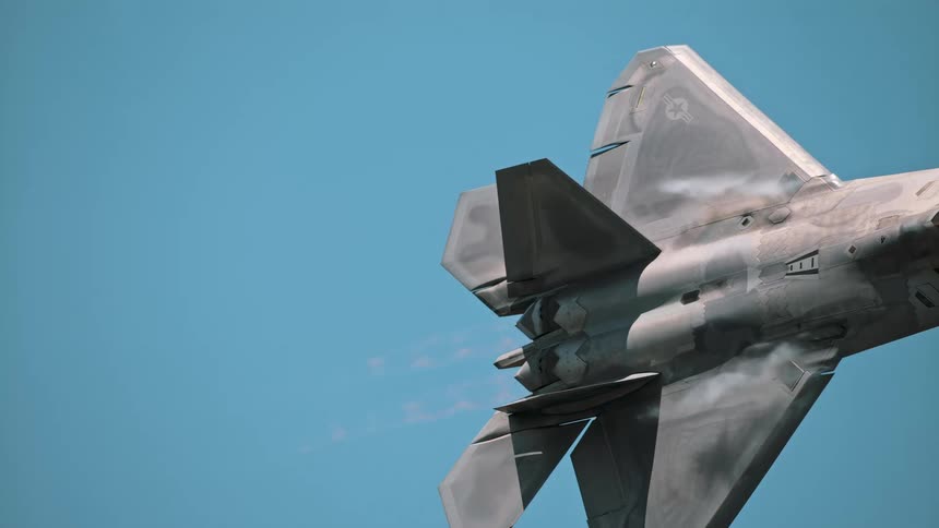 A slow-motion close-up of an F-22 Raptor fighter jet flying with vapor trails coming off its wings against a clear blue sky