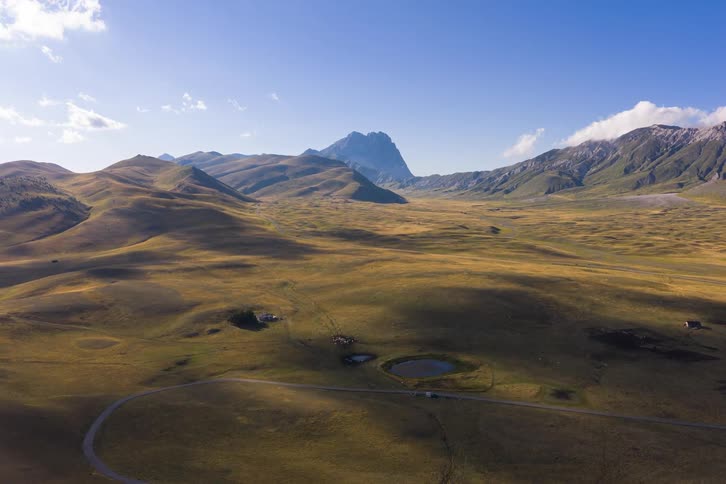 An aerial hyper-lapse reveals the vast, golden plains of Campo Imperatore as shadows dance across the landscape with the Gran Sasso mountain range in the distance