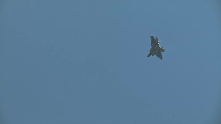 An F-22 Raptor fighter jet demonstrates its incredible maneuverability by performing a vertical climb and stall maneuver in slow motion against a clear blue sky