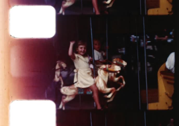Nostalgic home movie footage shows a little girl waving happily while riding a carousel at an amusement park