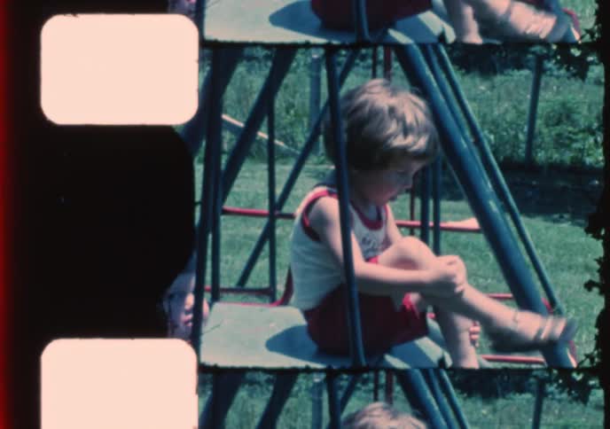 Vintage 8mm home movie footage shows two adorable toddlers playing together on a swing set in their backyard on a sunny day