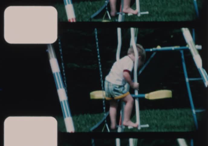 A nostalgic home movie from the 1970s shows a happy toddler playing on a swing set in his backyard on a sunny day